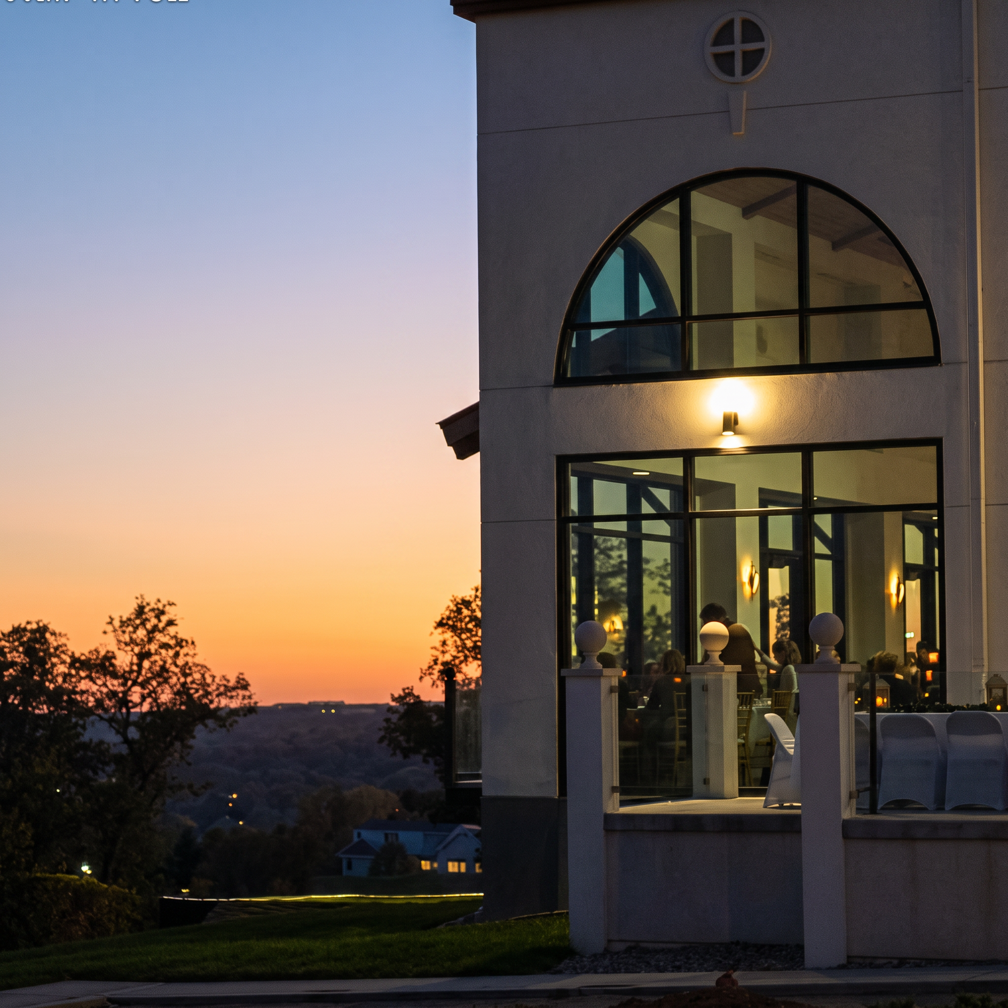 The Pinnacle at Westlake at sunset — a warmly lit arched window overlooking the Hill Country as guests dine inside.