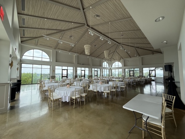 Empty ballroom set with round tables and gold chairs beneath the timbered ceiling.